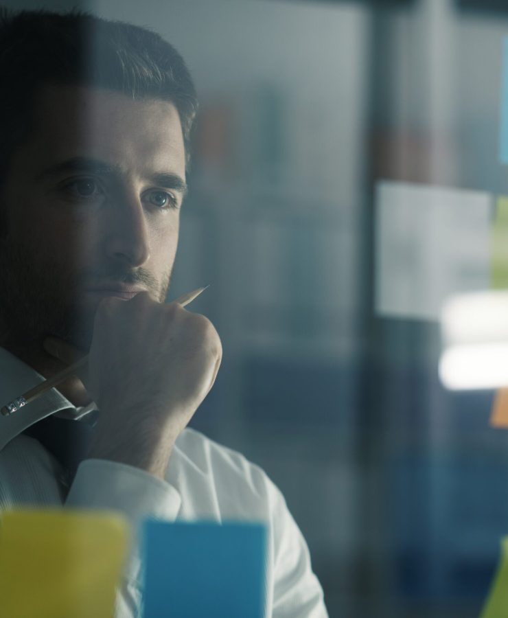 Business executive reading sticky notes on a glass, he is thinking about creative business solutions and strategies